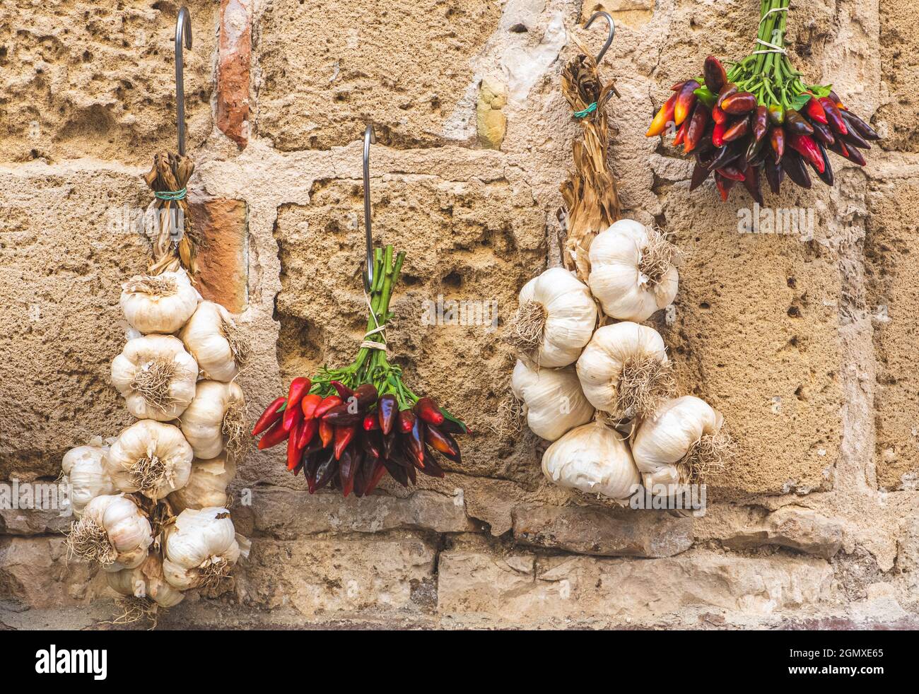 Mazzo di peperoncini caldi e aglio bianco fresco appeso su un muro di pietra in un mercato di Street food Foto Stock