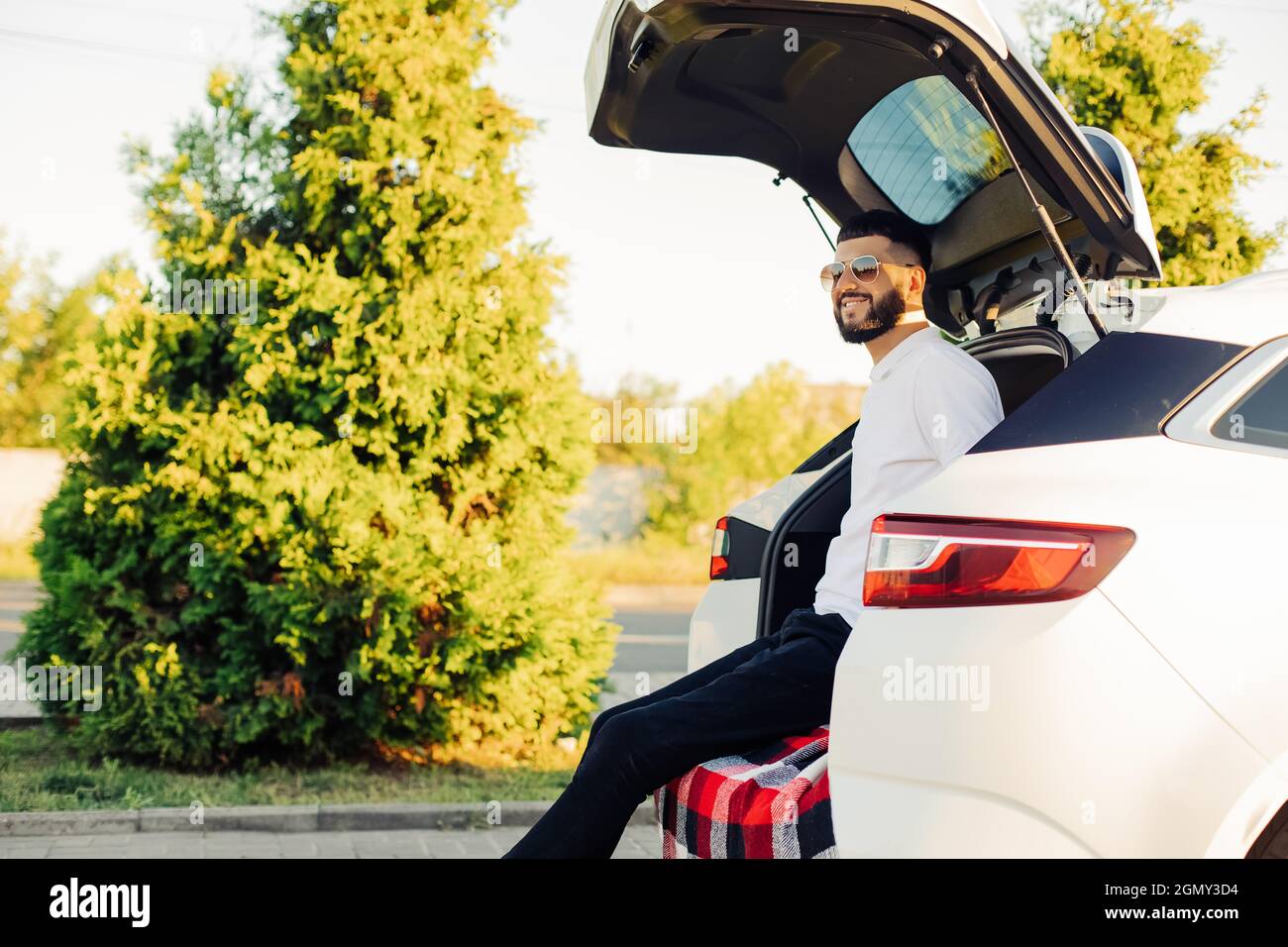 Felice uomo giovane in occhiali da sole, godendo il viaggio in auto, seduto nel bagagliaio della macchina, concetto di viaggio, vacanza estiva, vacanza Foto Stock
