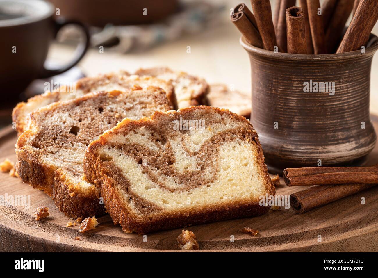 Primo piano di torta di pagnotta alla cannella a fette e bastoncini di cannella su un piatto di legno Foto Stock