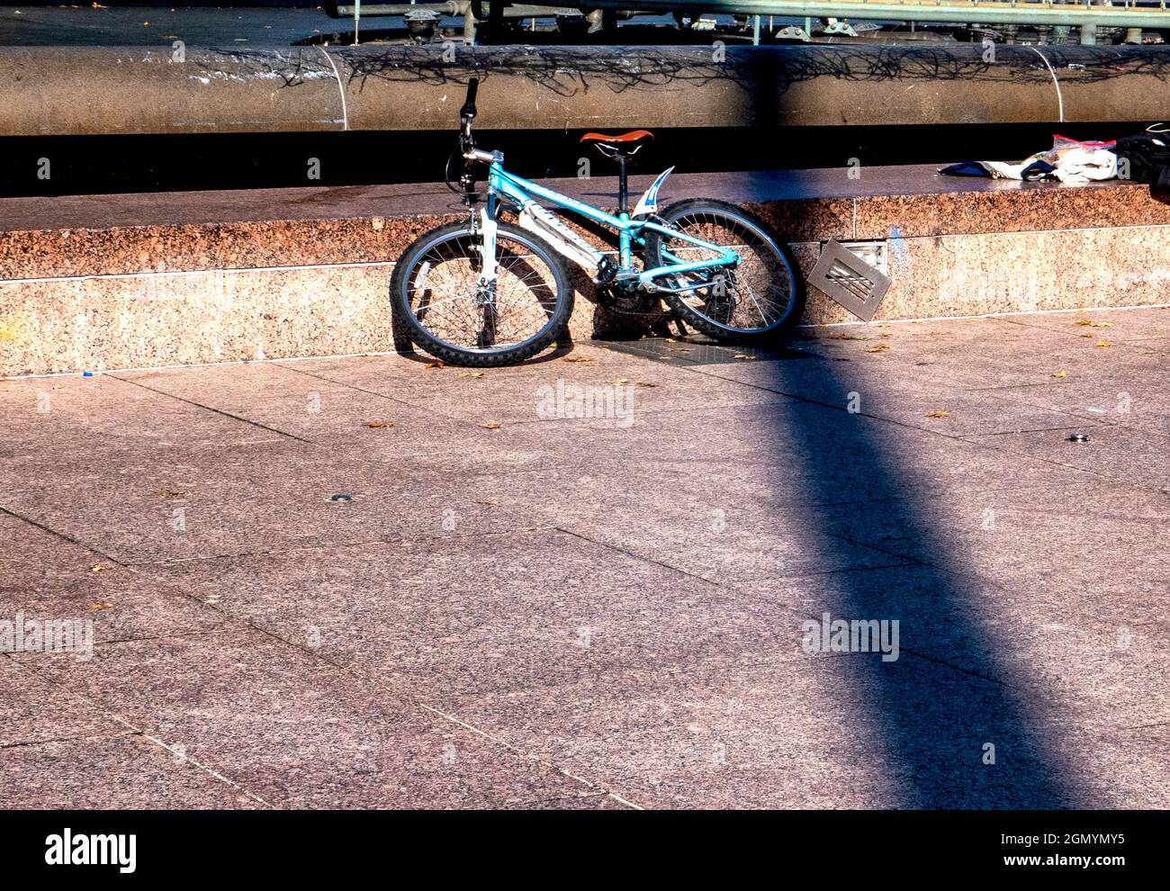 La bicicletta si appoggia contro una parete bassa all'ombra di un palo luminoso Foto Stock