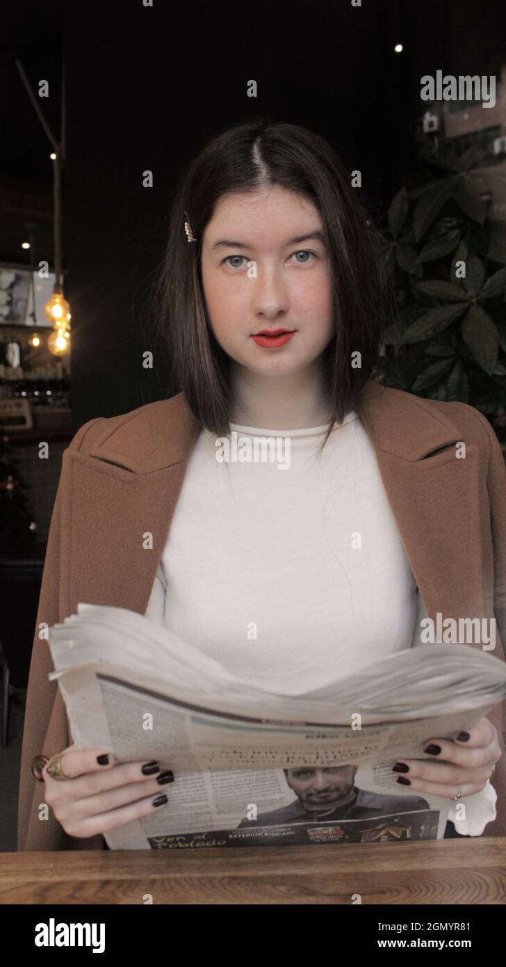 Giovane donna in un bar che tiene in mano il giornale e posa per la macchina fotografica. Autunno Vibes Concept 2021. Foto Stock
