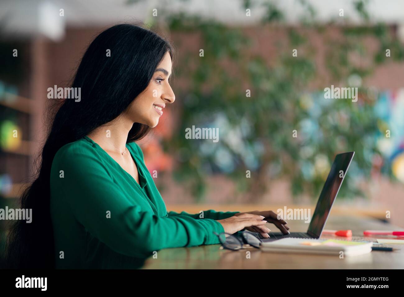 Vista laterale di donna bruna dai capelli lunghi usando il laptop, l'interno del caffè Foto Stock
