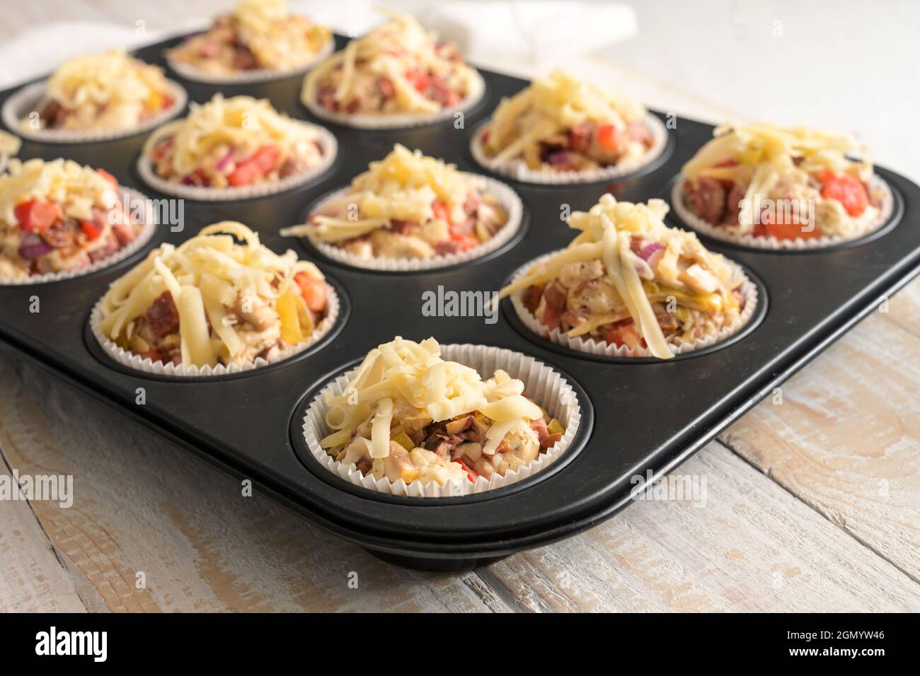 Muffin a base di lievito preparati con pomodori, verdure e formaggio in una teglia da forno pronta per il forno, fuoco selezionato, stretta profondità di fiel Foto Stock