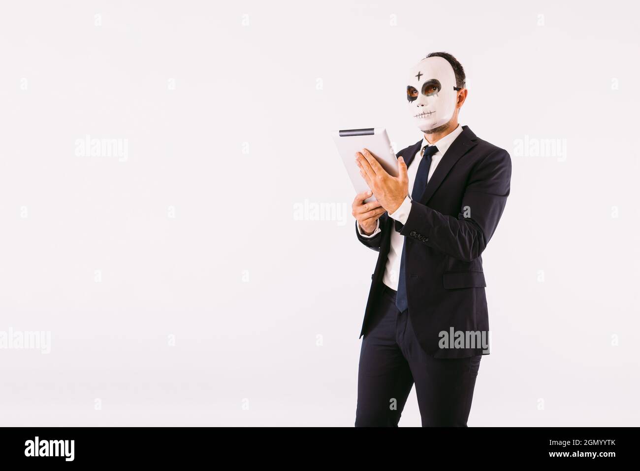 Uomo vestito di vestito e cravatta, indossando una maschera dell'assassino  con una croce sulla fronte per Halloween, guardando la sua tavoletta.  Carnevale e halloween celebrata Foto stock - Alamy