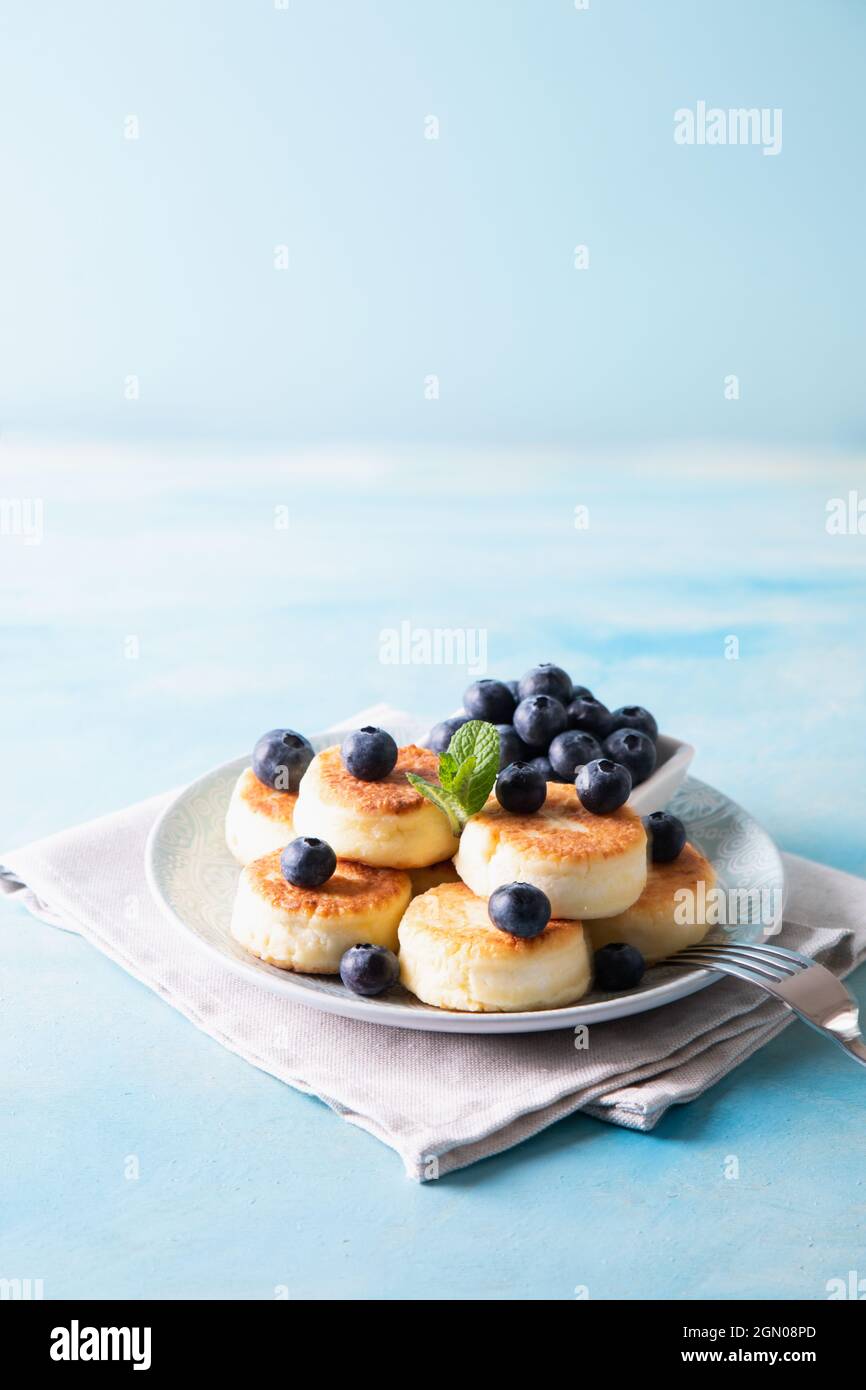 Frittelle di formaggio cottage. Cheesecakes dal formaggio di cottage, deliziosa colazione, tradizionali frittelle dolci russe. Con mirtillo, menta e miele. Foto Stock