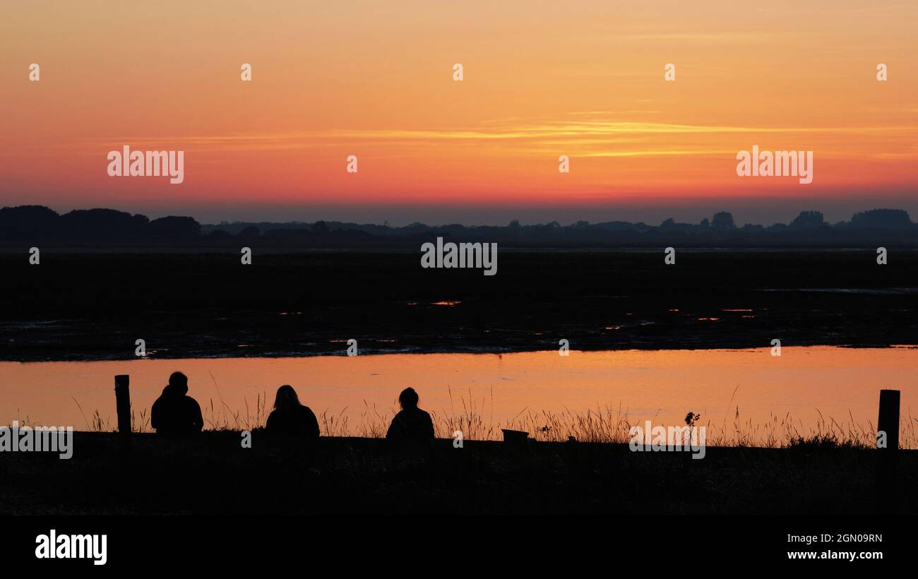 Tre persone hanno visto guardare il tramonto a Pagham, Regno Unito. Foto Stock