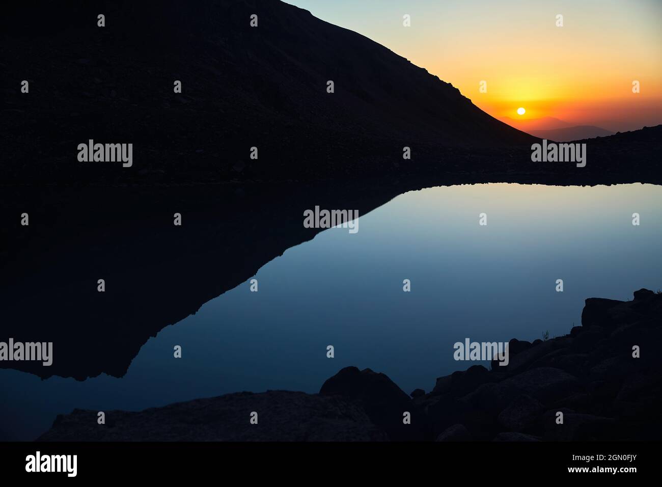 Splendido scenario di grande lago e silhouette di montagne al tramonto bagliore luce nelle montagne di Tien Shan, Kazakistan. Foto Stock