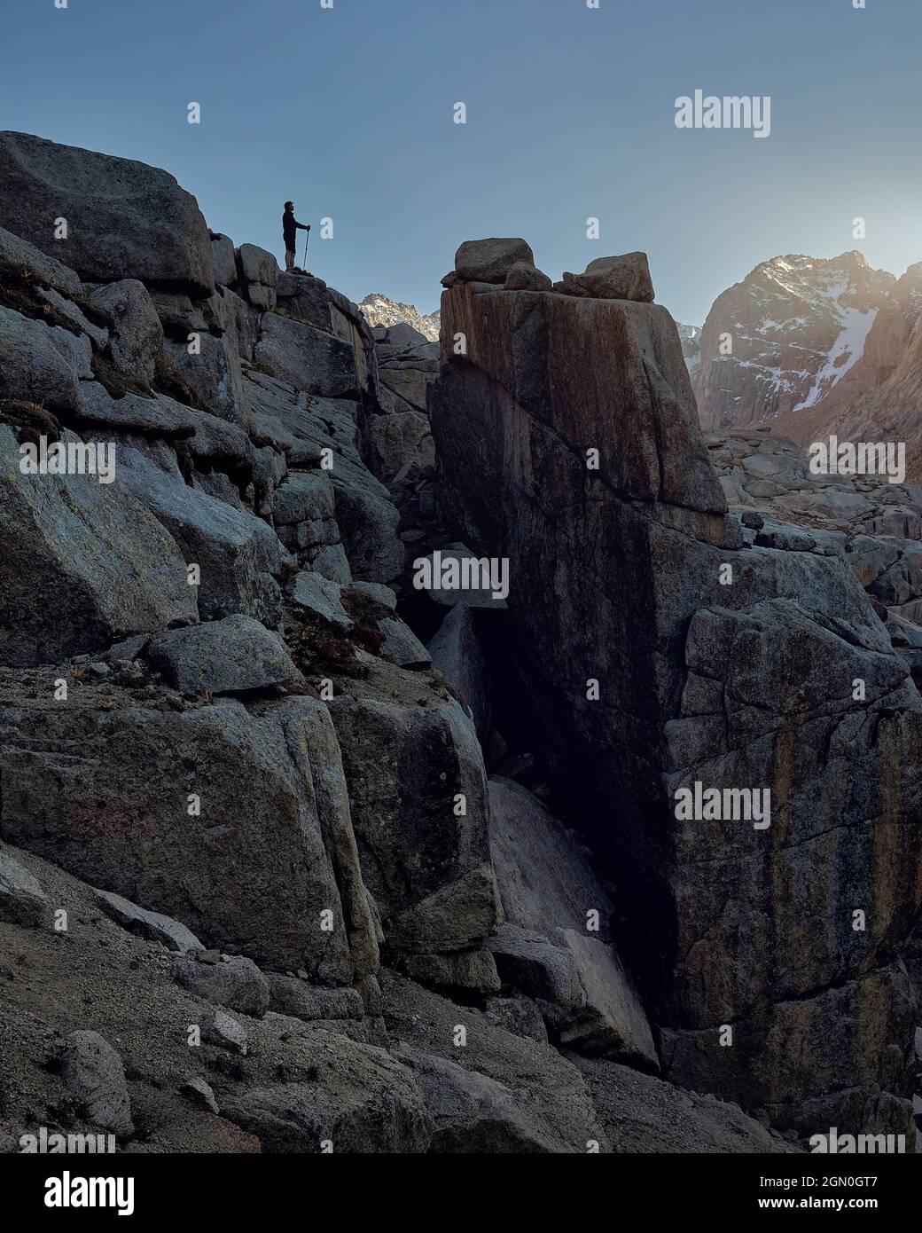 Silhouette di uomo Hiker turista in piedi sulla roccia alta contro la valle di montagna neve. Concetto all'aperto e trekking. Foto Stock
