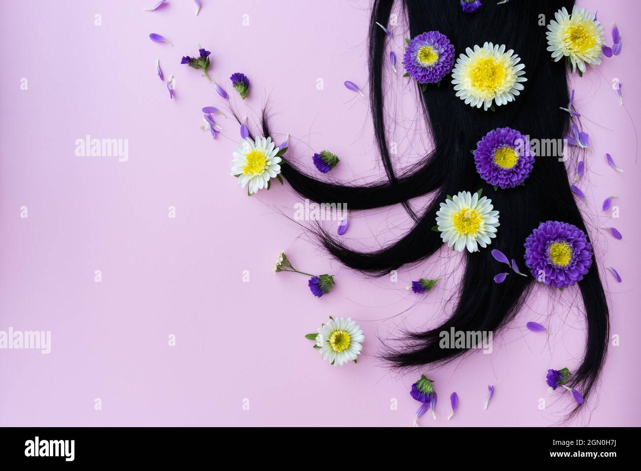 Capelli neri con fiori gialli e lilla e petali su di esso. Concetto di cura dei capelli. Foto Stock