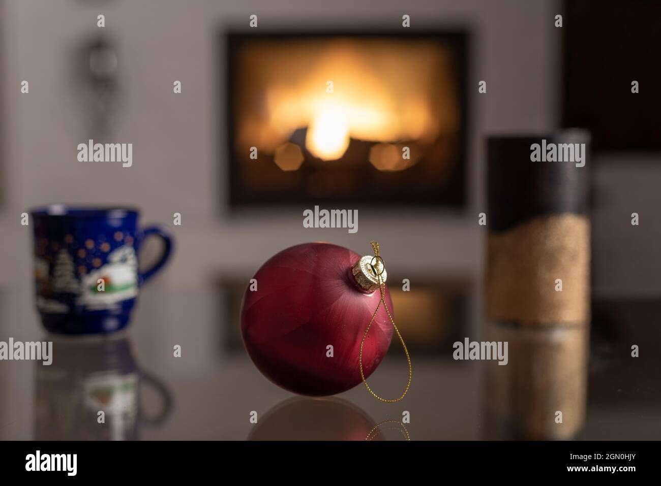 Bel giocattolo albero di natale su un tavolo di vetro, camino e tazza di Natale sullo sfondo Foto Stock