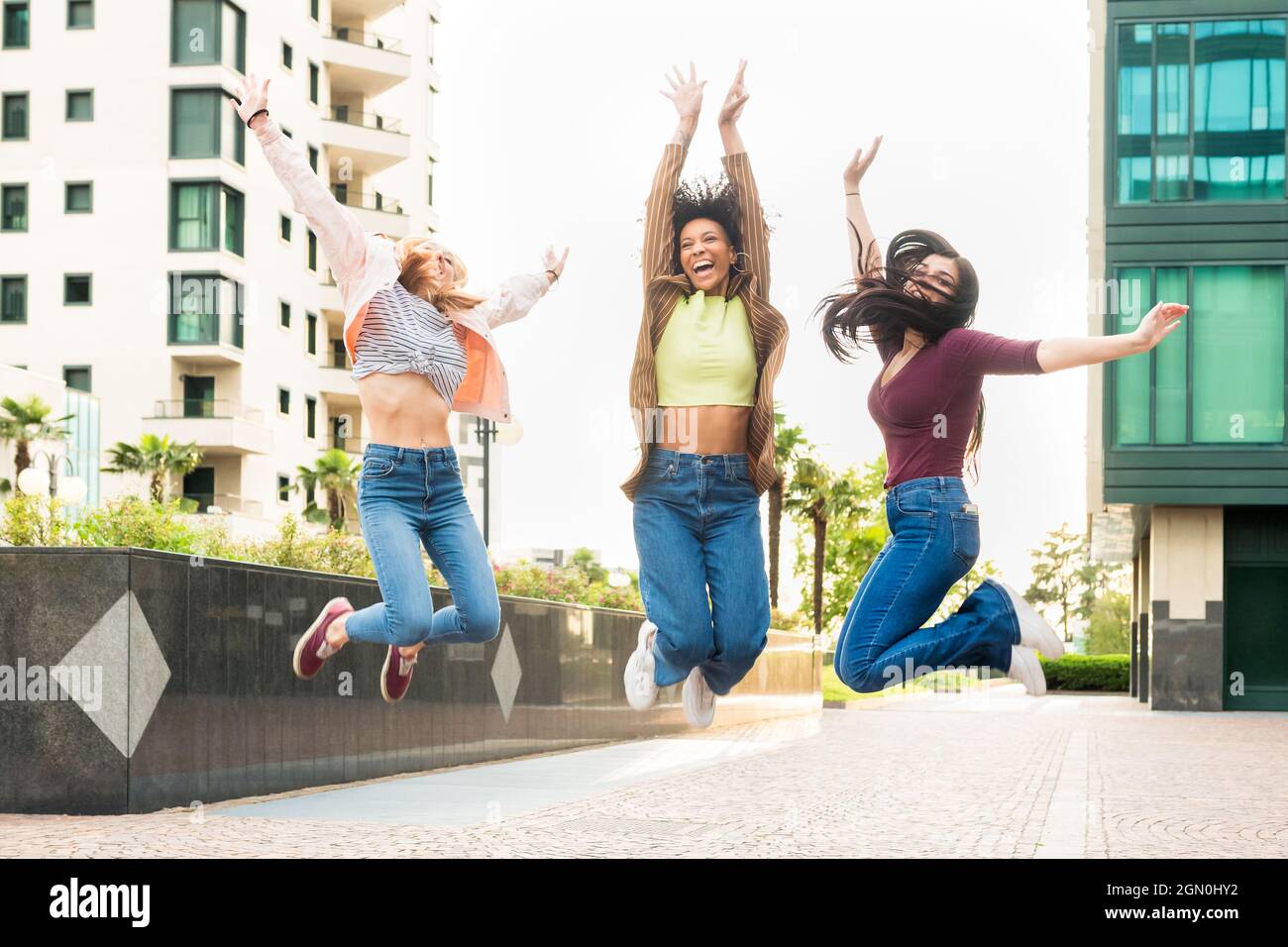Tre esuberante giovane donna felice che festeggia saltando in aria insieme ridendo e rallegrandosi in una strada della città Foto Stock