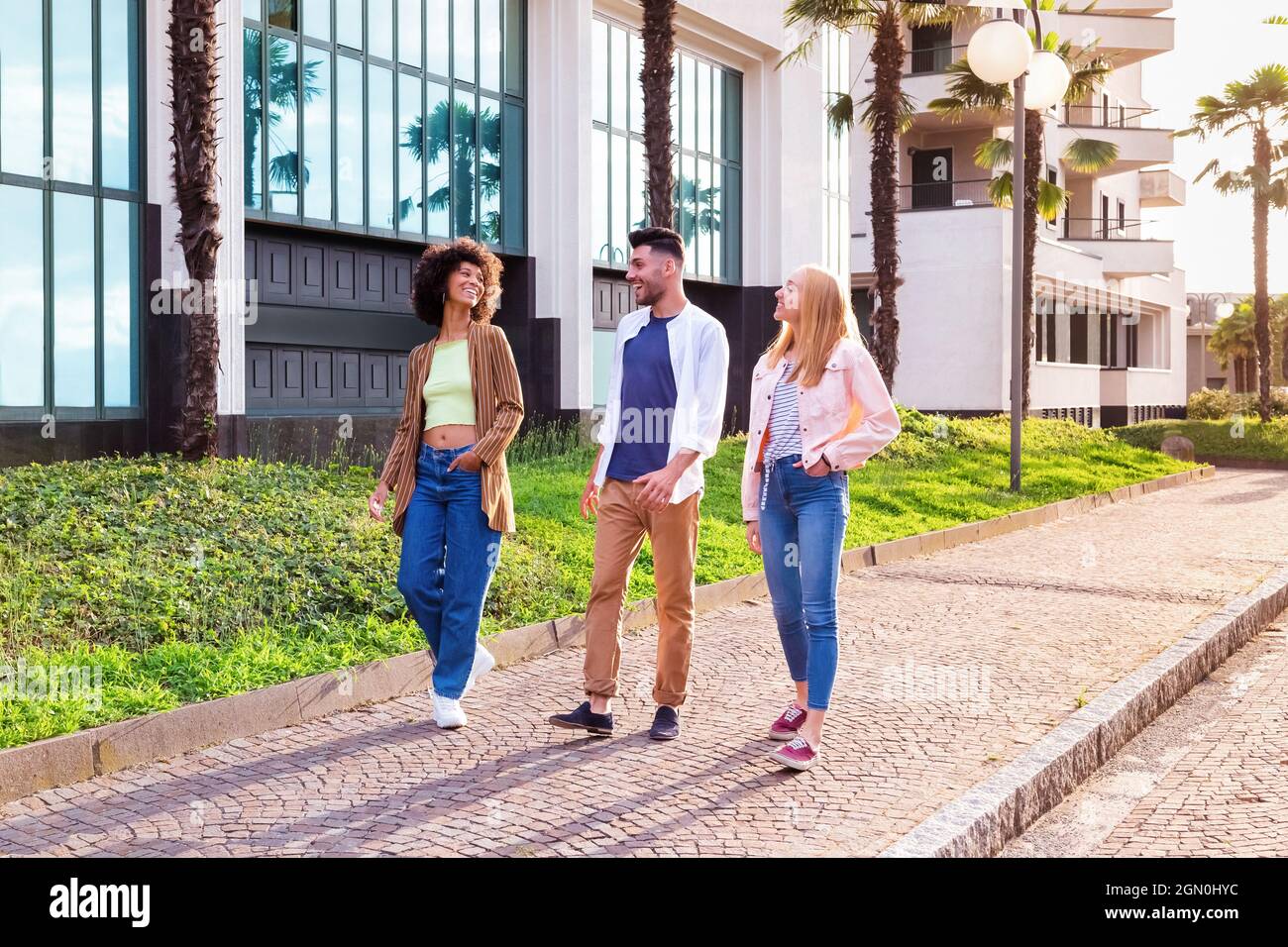 Corpo pieno di giovani studenti allegri multirazziali in abiti casual alla moda chiacchierando e ridendo amichevole mentre passeggi insieme sul marciapiede vicino mod Foto Stock