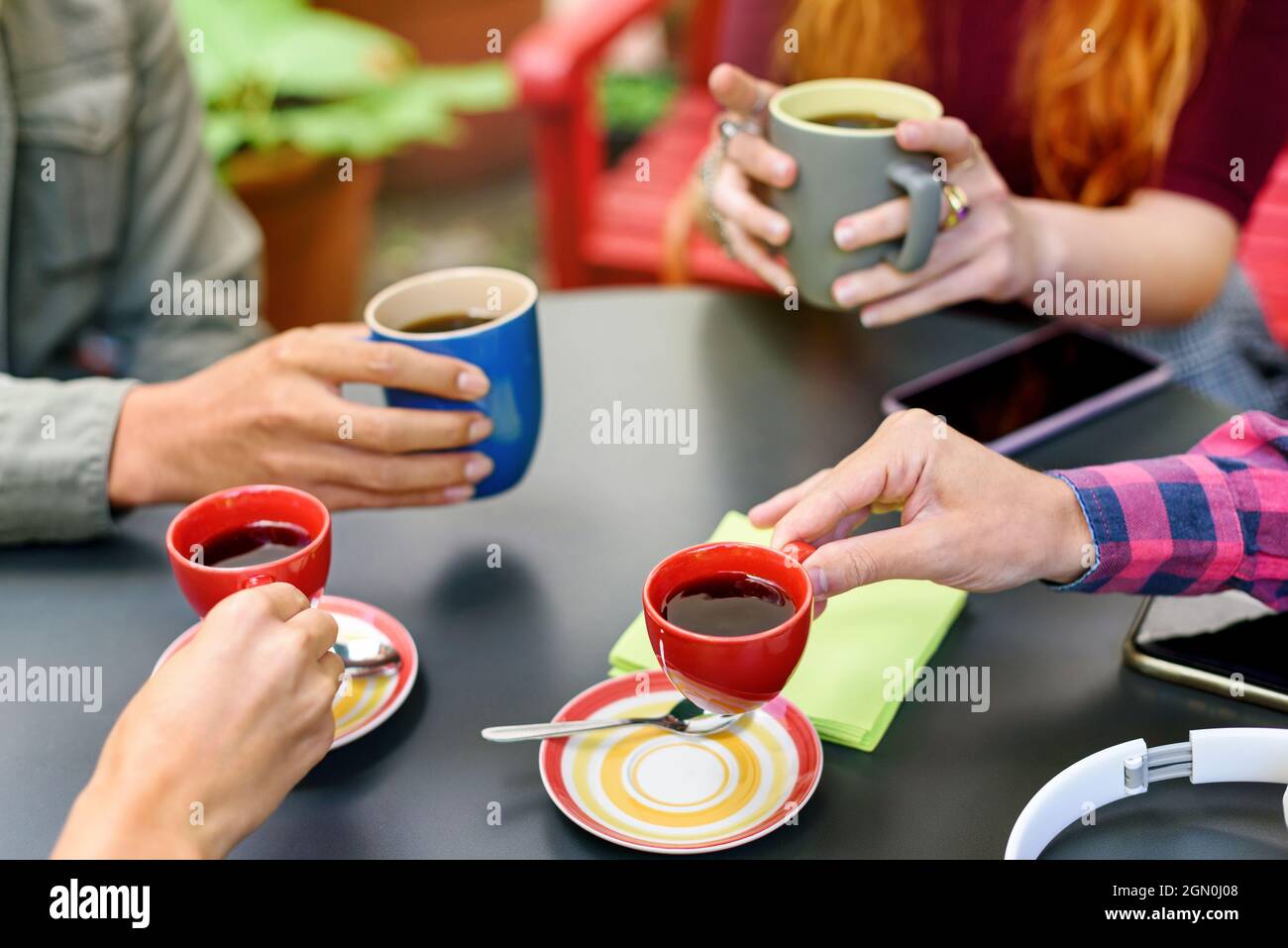 Gruppo di giovani amici che si godono una pausa caffè insieme in un primo piano sulle loro mani seduti intorno a un tavolo che tiene tazze e tazze di caffè nero Foto Stock