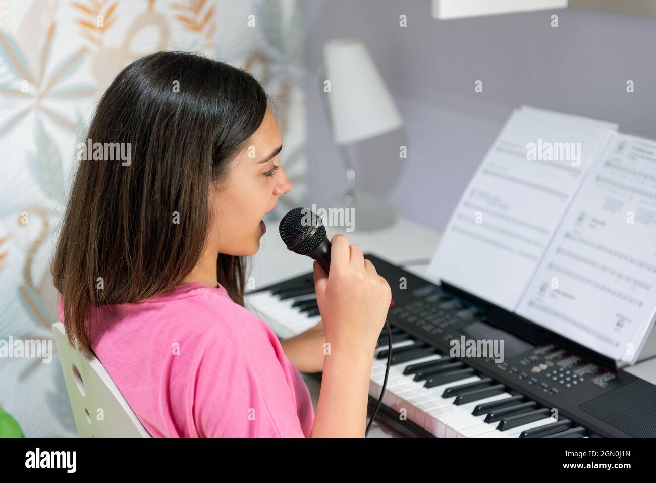 Vista laterale di teen girl di talento con microfono che suona la canzone e il pianoforte elettrico durante il tempo libero a casa Foto Stock