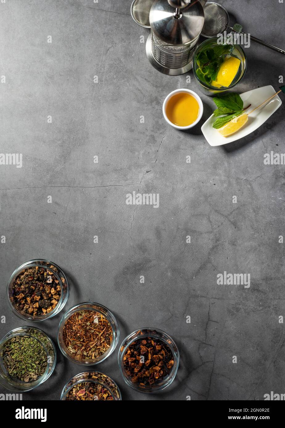 Layout creativo con tè, tè verde, tè nero e vari tipi di frutta e tisane su sfondo di pietra scura. Posa piana. Foto Stock