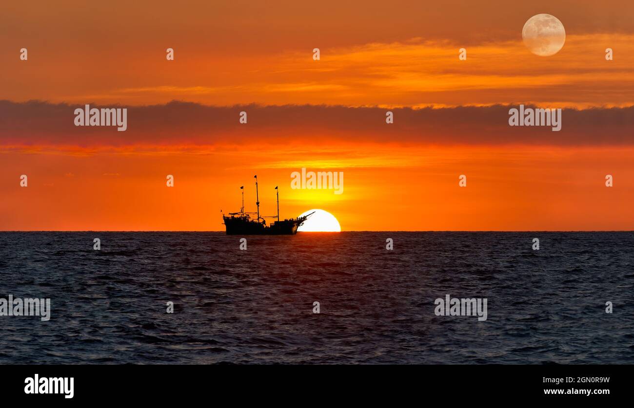 Una nave dei pirati si trova sull'oceano e si trova contro UNA Cielo arancione colorato al tramonto Foto Stock