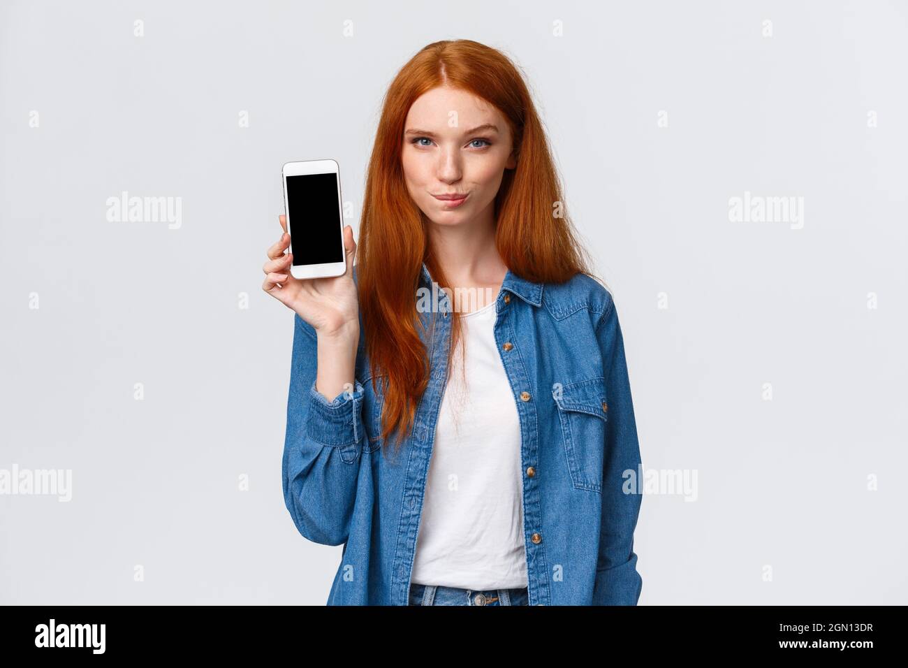 Sassy e audace donna rosso-guardare che ha un piano interessante, mostrando la sua lista dei desideri in modo da sapere che cosa comprare sul display dello smartphone, lecca labbra tentazione Foto Stock