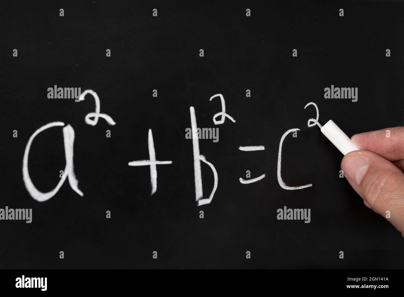 Un insegnante scrive l'equazione del teorema pitagorico su una lavagna nera mentre insegna un gruppo di studenti in un'aula. Foto Stock