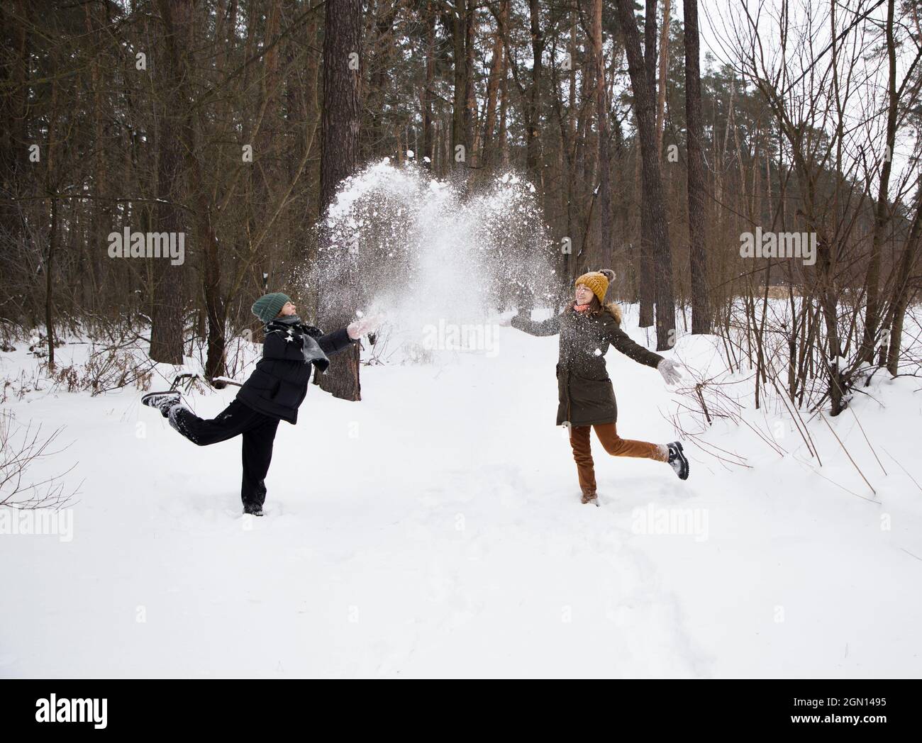 due giovani donne in abiti caldi si divertono a giocare all'aria aperta in inverno e lanciano una soffice neve l'una sull'altra. Ciao inverno, buone feste di natale, digitale Foto Stock