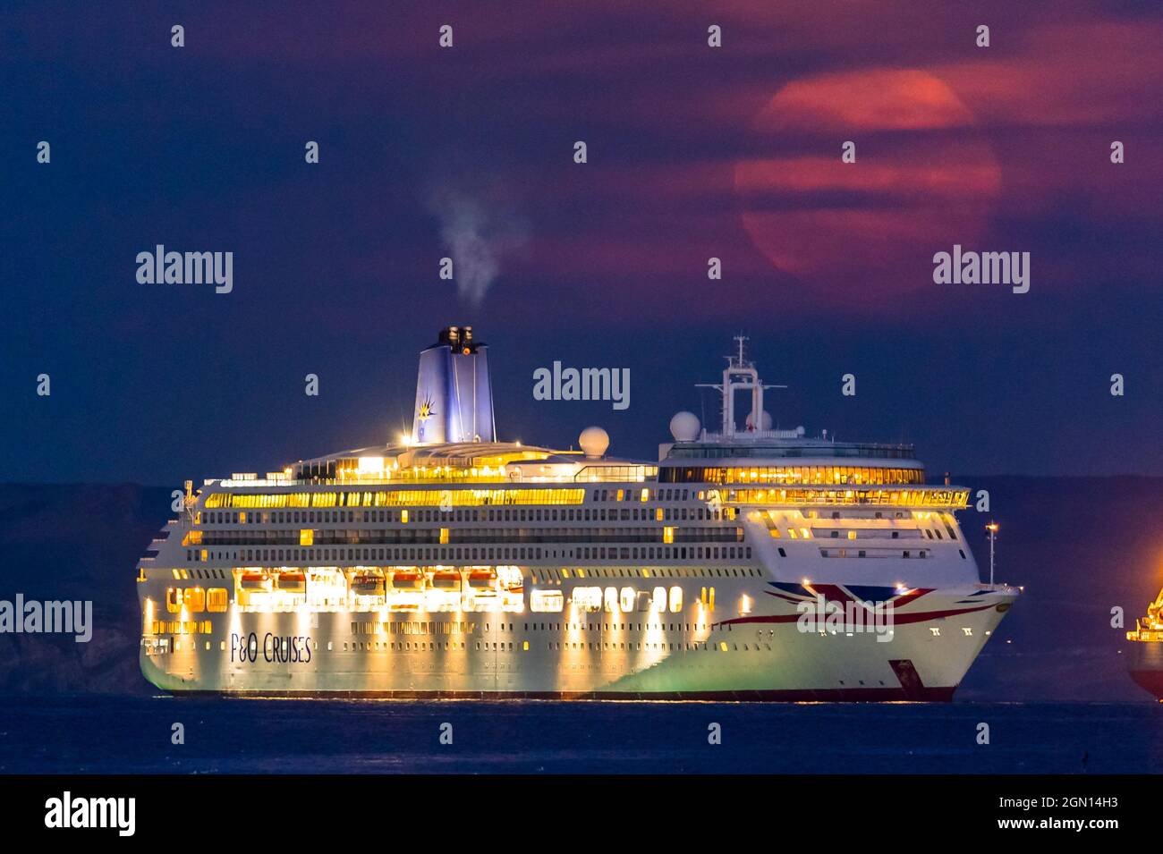 Weymouth, Dorset, Regno Unito. 21 settembre 2021. Meteo Regno Unito. La Luna piena di Harvest è oscurata da sottili alte nuvole come si alza da dietro la nave da crociera P&o Aurora che è ancorata nella baia a Weymouth in Dorset il l'ultimo giorno di estate astronomica. Picture Credit: Graham Hunt/Alamy Live News. Foto Stock