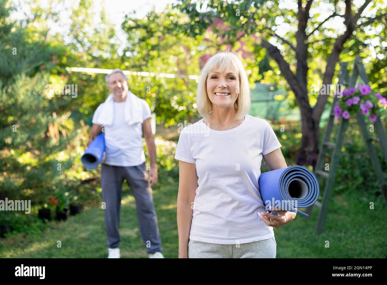 Sano stile di vita pensionamento. Coppia attiva e felice che tiene stuoie yoga, guardando la macchina fotografica in giardino soleggiato Foto Stock