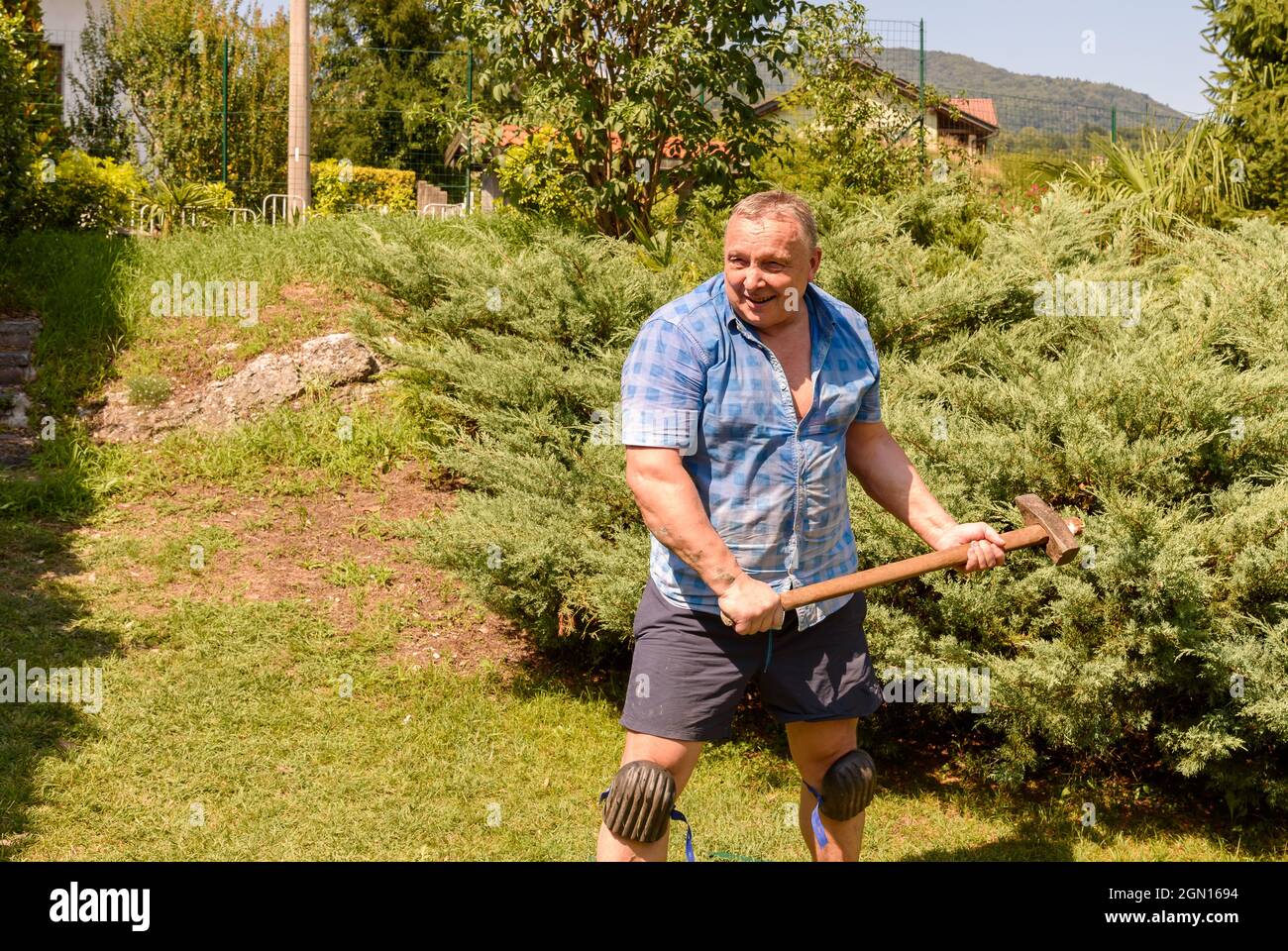 Uomo maturo e muscoloso con martello in giardino. Foto Stock