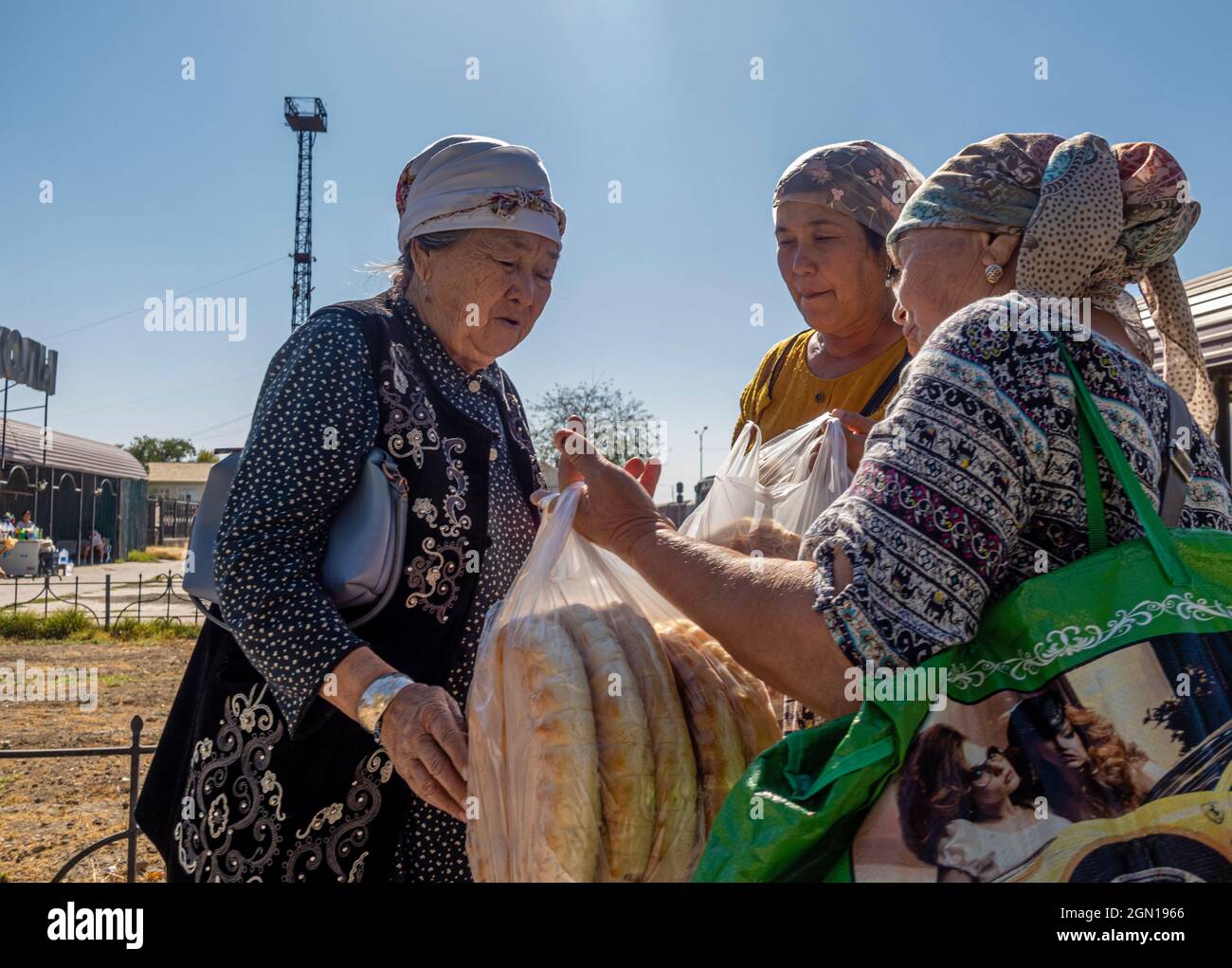 Donne in abbigliamento tradizionale che vendono pane rotondo (lepeshka) alla fermata per i passeggeri del treno, Kyzyl-Orda, Kazakhstan, Asia centrale Foto Stock
