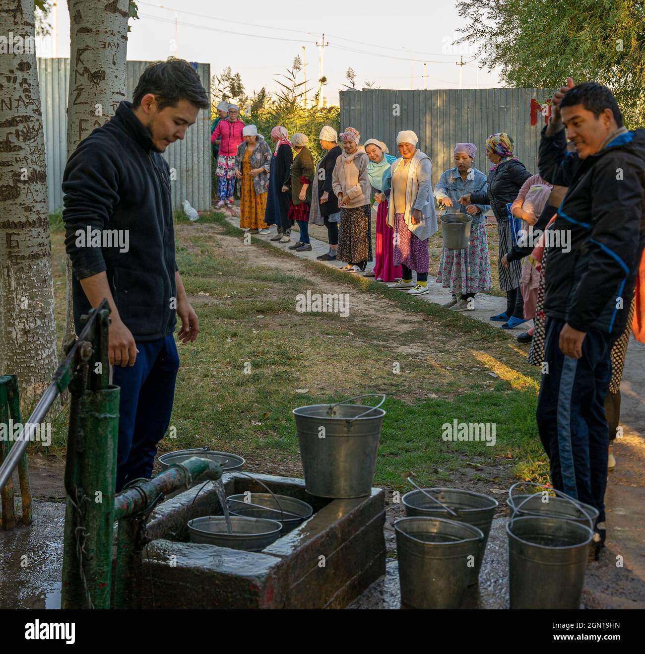 Gli uomini kazaki che disegnano l'acqua da un pozzo e passano i secchi alle donne per l'affusione. Si ritiene che l'acqua sia Santa e guaritrice; il Turkistan. Foto Stock