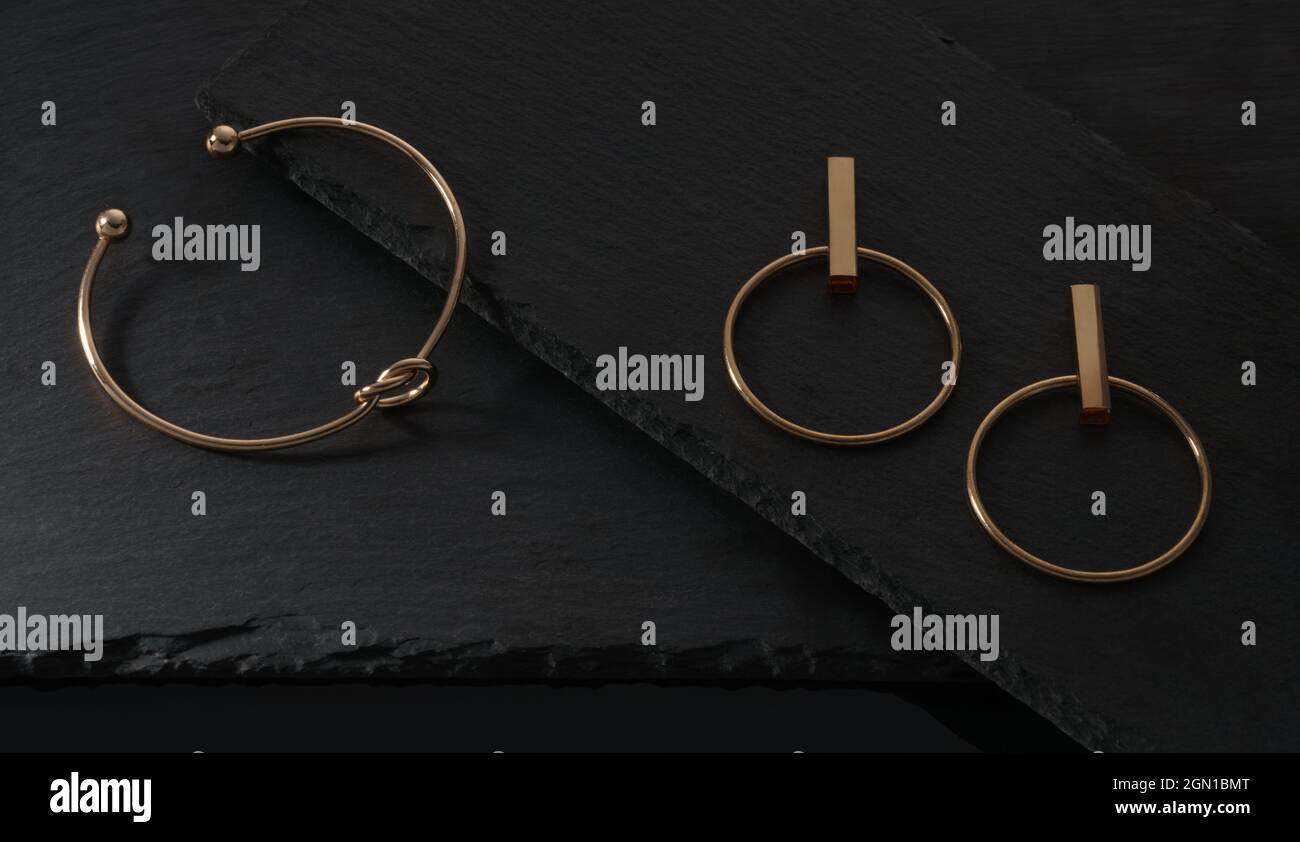 Vista dall'alto del bracciale e degli orecchini dorati a forma di Knot su piastre nere Foto Stock
