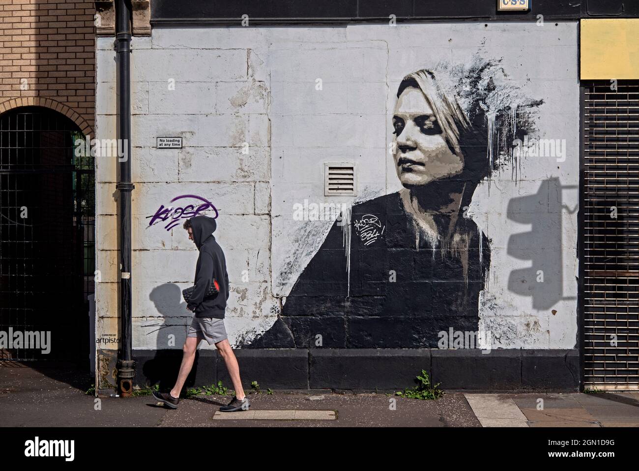 Giovane uomo che cammina da Donna in Nero di James Klinge a Bridgegate, parte del percorso murale di Glasgow. Foto Stock
