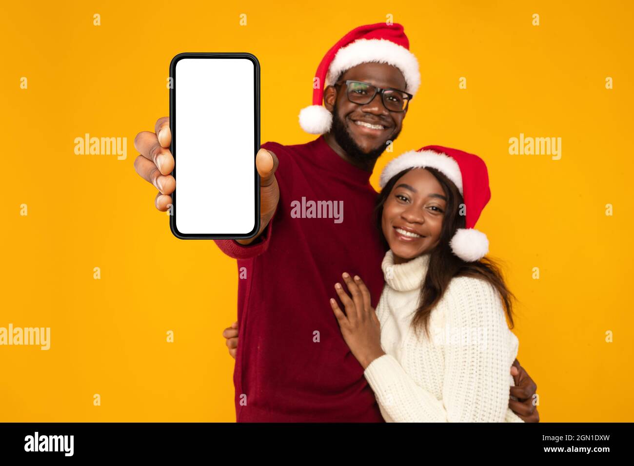 Coppia nera in Babbo Natale con schermo del telefono, sfondo giallo Foto Stock