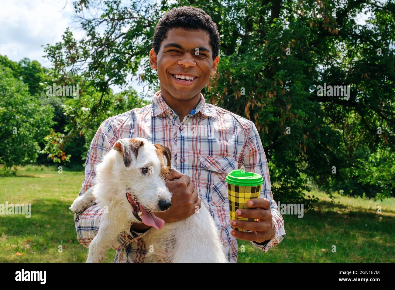 L'uomo afro americano tiene un cane Jack Russell e beve il caffè da una tazza di carta Foto Stock