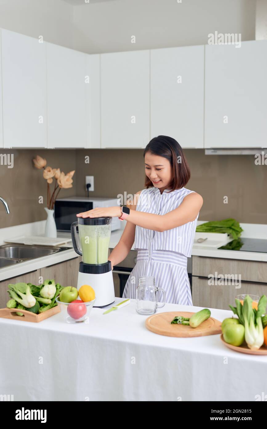 Vegano sorridente donna asiatica facendo un frullato con frutta e verdura in cucina Foto Stock