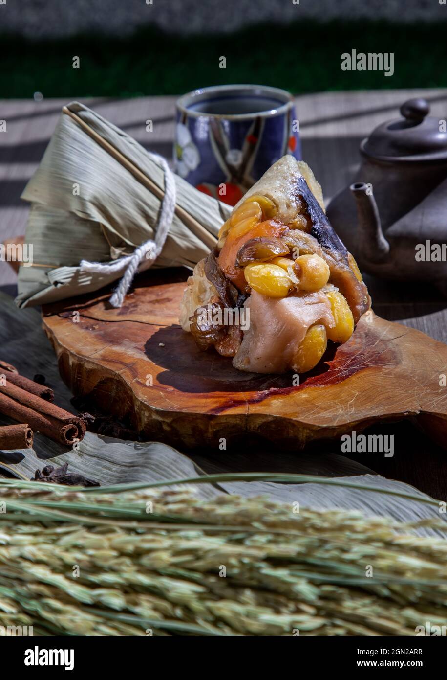 Gnocchi di riso cinese (Zongzi) a forma di piramide avvolto da foglie ingredienti su piatto di legno servito con tè cinese. Famoso foo asiatico gustoso fatto a mano Foto Stock