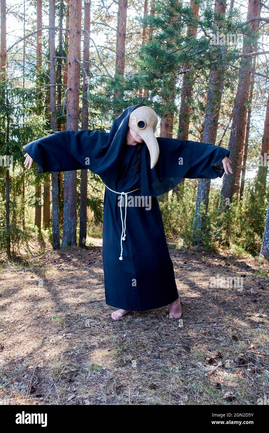 Un uomo in una maschera medico peste si erge nella foresta contro gli alberi di sfondo Foto Stock