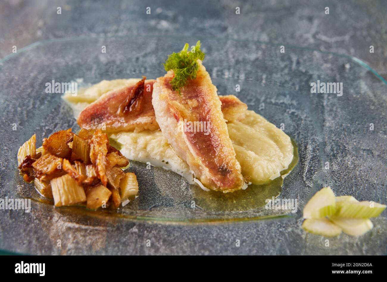 Pezzi di pesce Barbunya con finocchio e salsa su piatto di vetro. Foto Stock