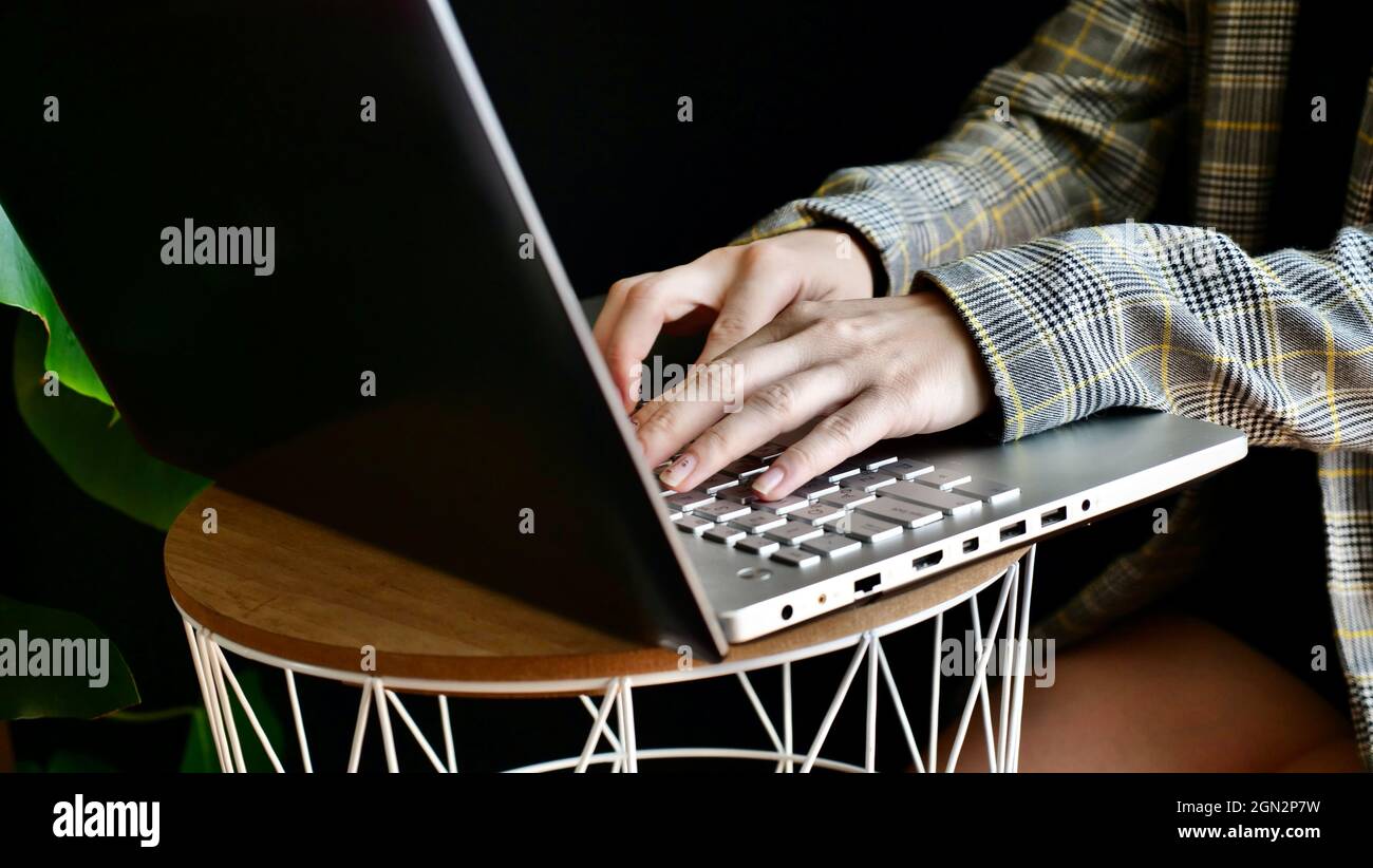 Primo piano delle mani della donna in una giacca che digita su un computer portatile. La persona lavora, studia a casa online. Nessuna faccia. Foto Stock