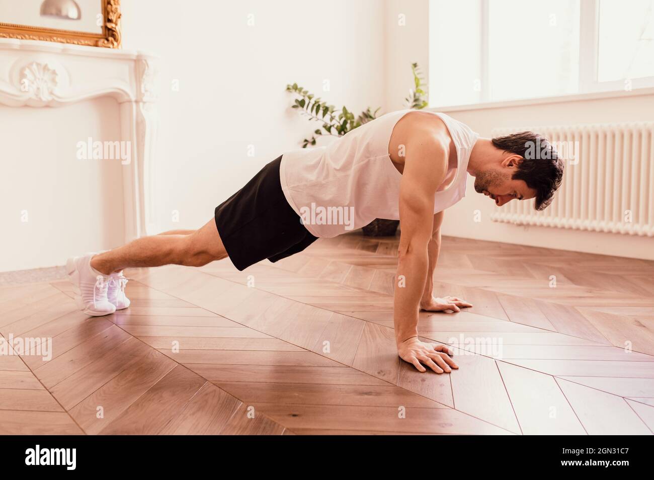 Bell'uomo muscoloso in una t-shirt e pantaloncini che fanno esercizi funzionali sul pavimento a casa Foto Stock