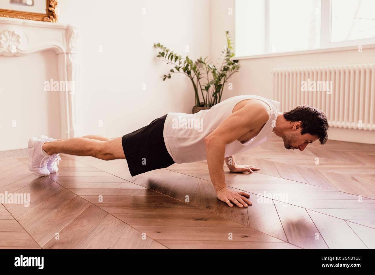 Bell'uomo muscoloso in una t-shirt e pantaloncini che fanno esercizi funzionali sul pavimento a casa Foto Stock