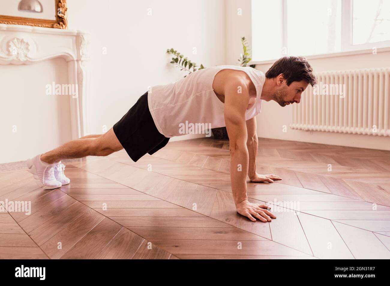 Bell'uomo muscoloso in una t-shirt e pantaloncini che fanno esercizi funzionali sul pavimento a casa Foto Stock