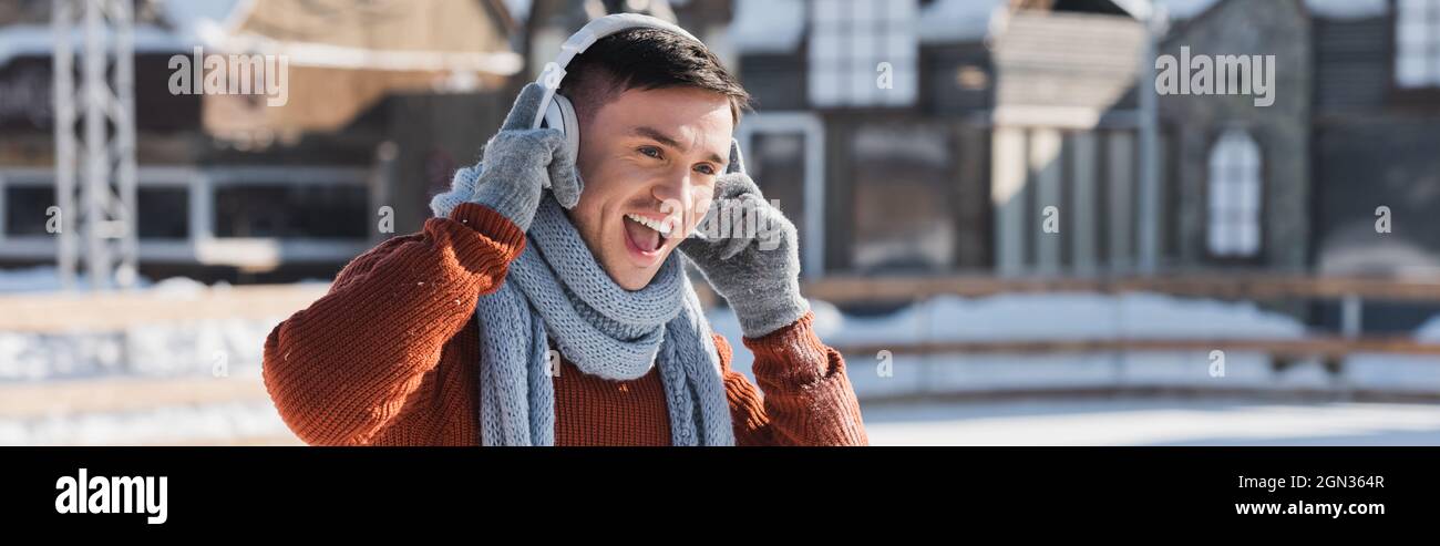 giovane uomo positivo in maglione e sciarpa ascoltando musica mentre cantano all'esterno, banner Foto Stock