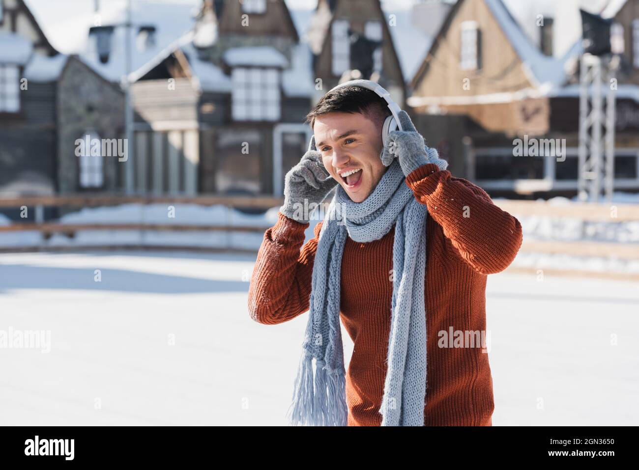 felice giovane uomo in maglione e sciarpa ascoltando musica mentre cantano all'esterno Foto Stock