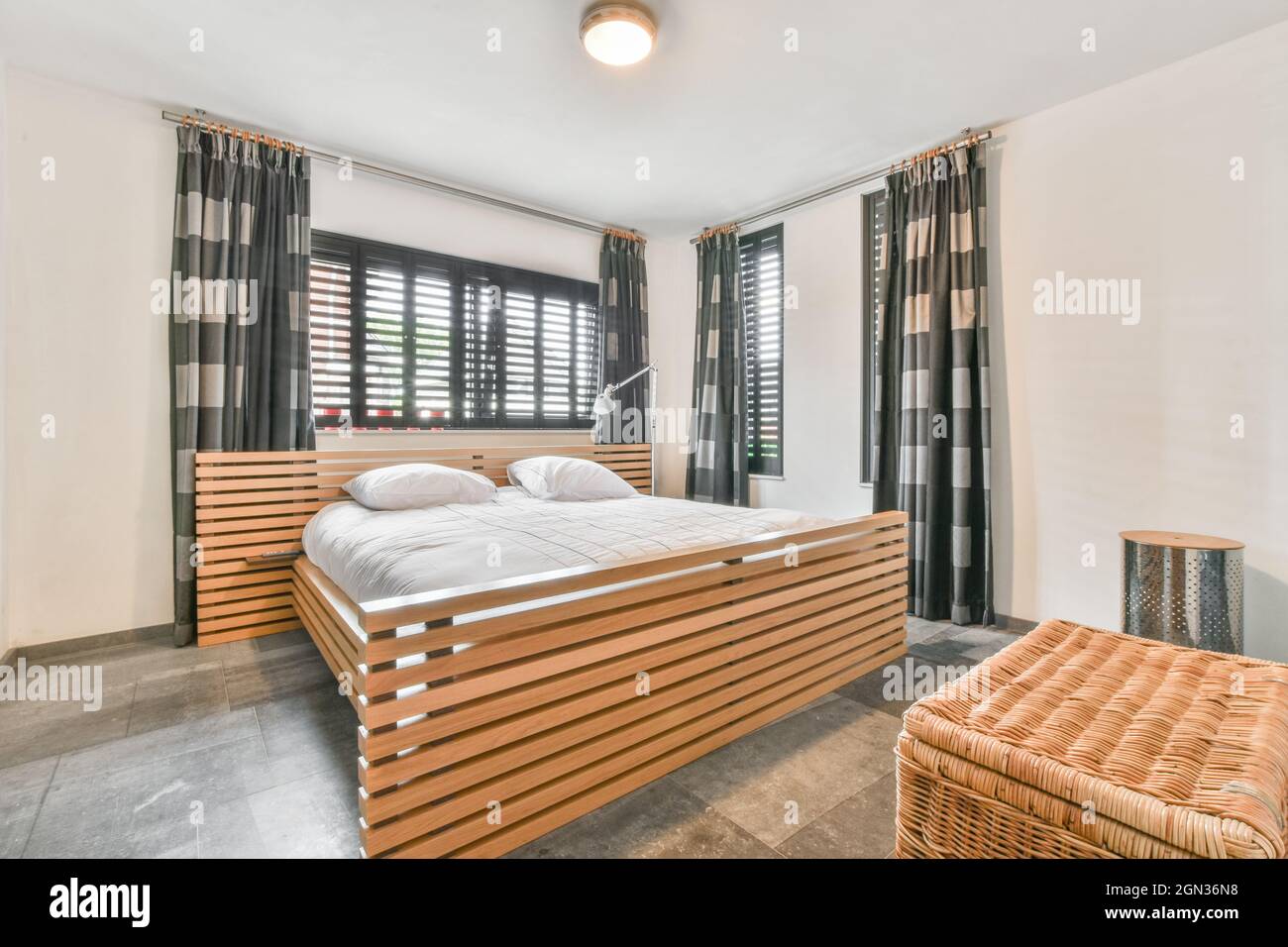 Moderna camera da letto interna con letto con cuscini sotto lampada luminosa sul soffitto dell'appartamento Foto Stock