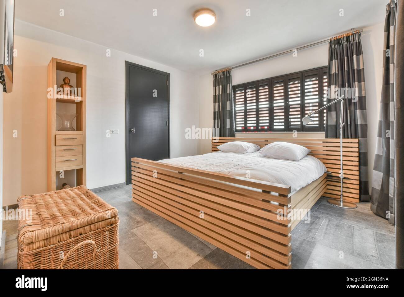 Moderna camera da letto interna con letto con cuscini sotto lampada luminosa sul soffitto dell'appartamento Foto Stock