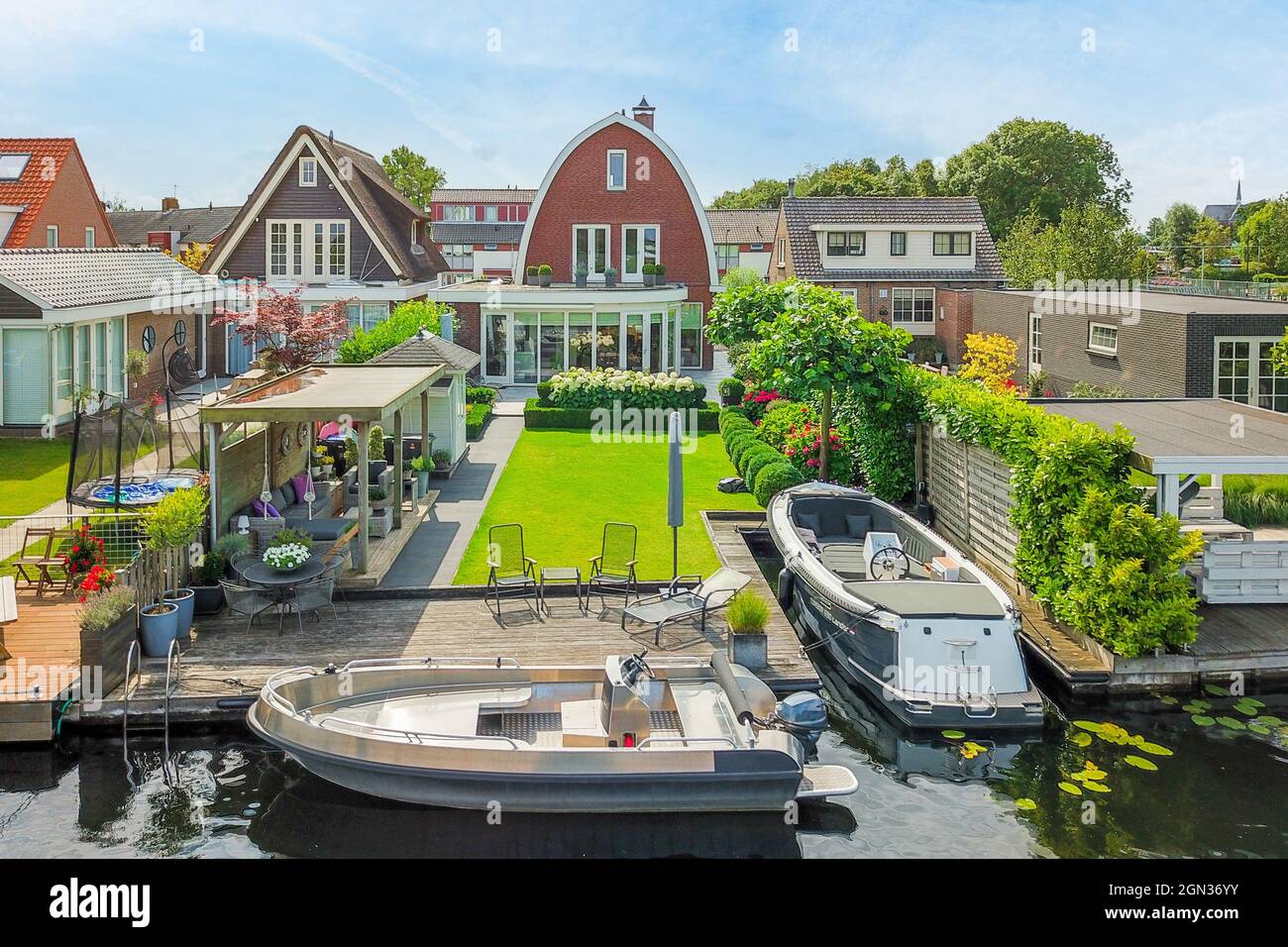 Barche a motore ormeggiate sul fiume tra facciate residenziali e piante sotto cielo nuvoloso in provincia di Utrecht Olanda Foto Stock