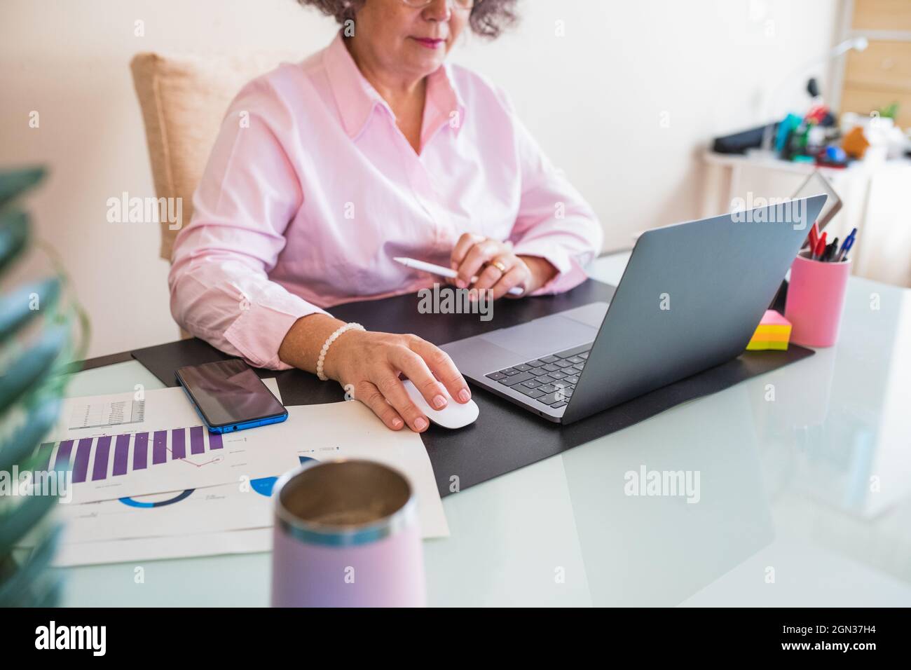 Ritagliare l'imprenditore femminile senior con tablet e netbook che lavorano alla scrivania con grafica su fogli di carta Foto Stock