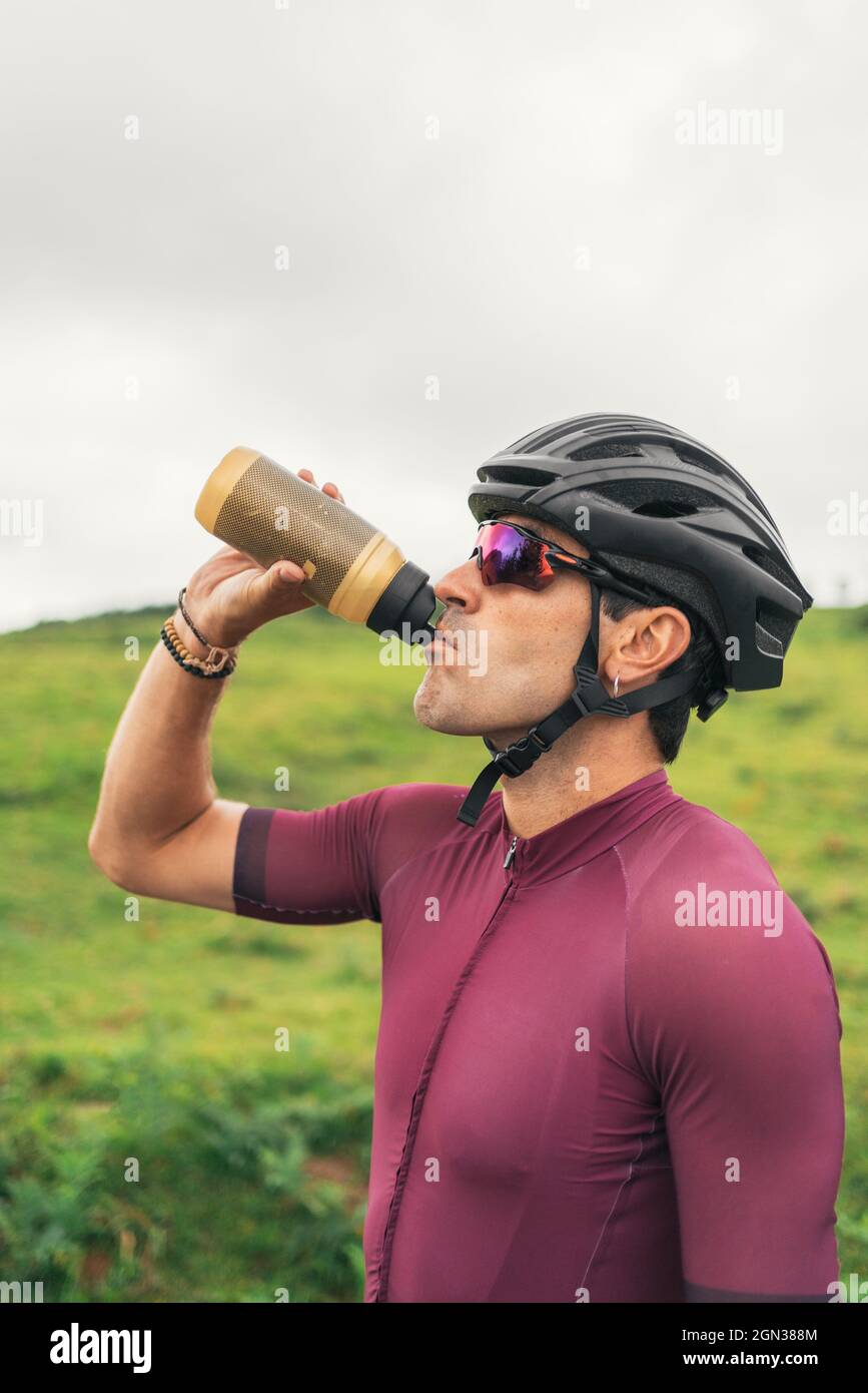 Vista laterale dello sportivo in casco da ciclismo e occhiali da sole che  bevono acqua dalla bottiglia durante la pausa dall'allenamento Foto stock -  Alamy
