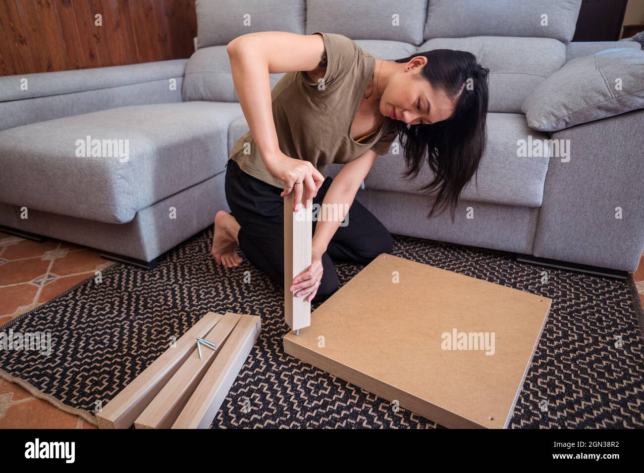 Focalizzata giovane asiatica femmina che fissa gamba tavolo al tavolo su tappeto ornamentale in casa di luce Foto Stock