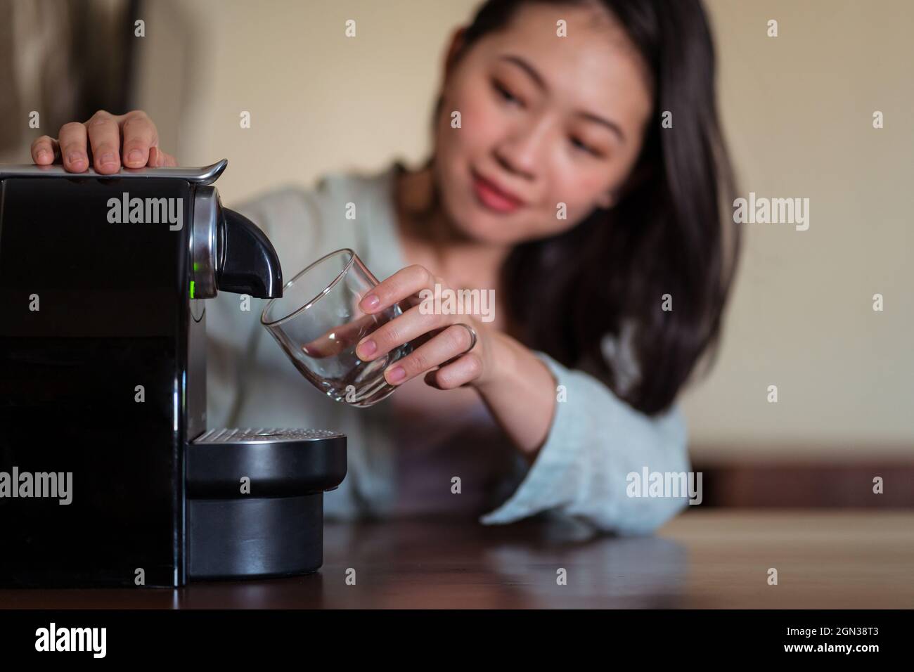 Giovane etnia femminile contro cialde macchina caffè versando bevande calde con schiuma in vetro in cucina casa Foto Stock