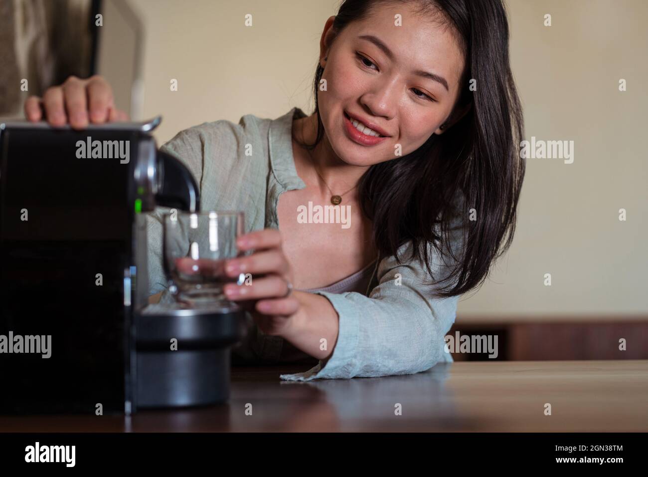 Giovane etnia femminile contro cialde macchina caffè versando bevande calde con schiuma in vetro in cucina casa Foto Stock